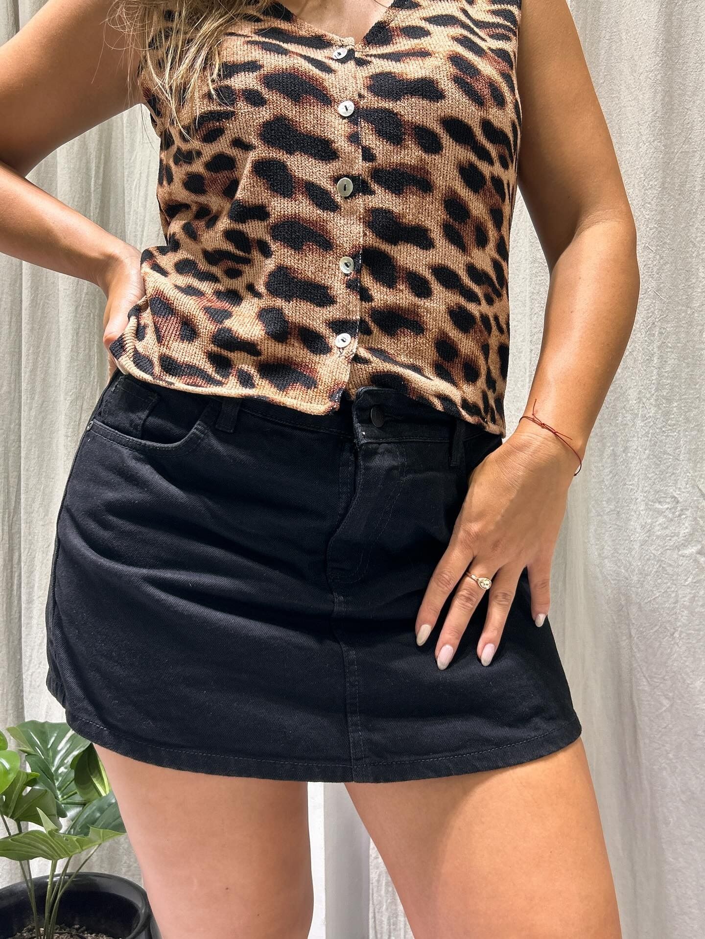 Mujer con top estampado de leopardo y falda vaquera negra, posando en interiores.
