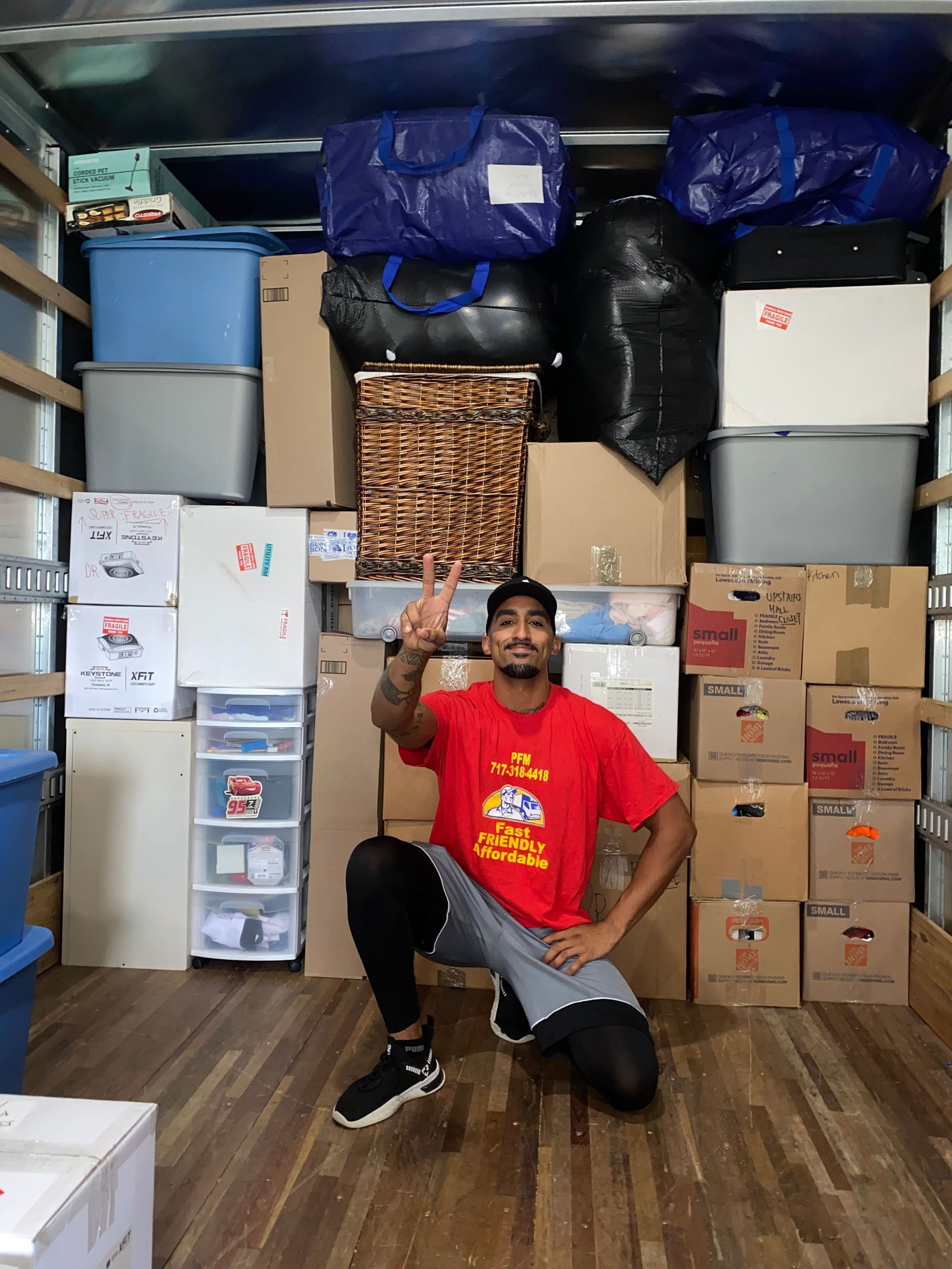A man is kneeling in the back of a moving truck filled with boxes.