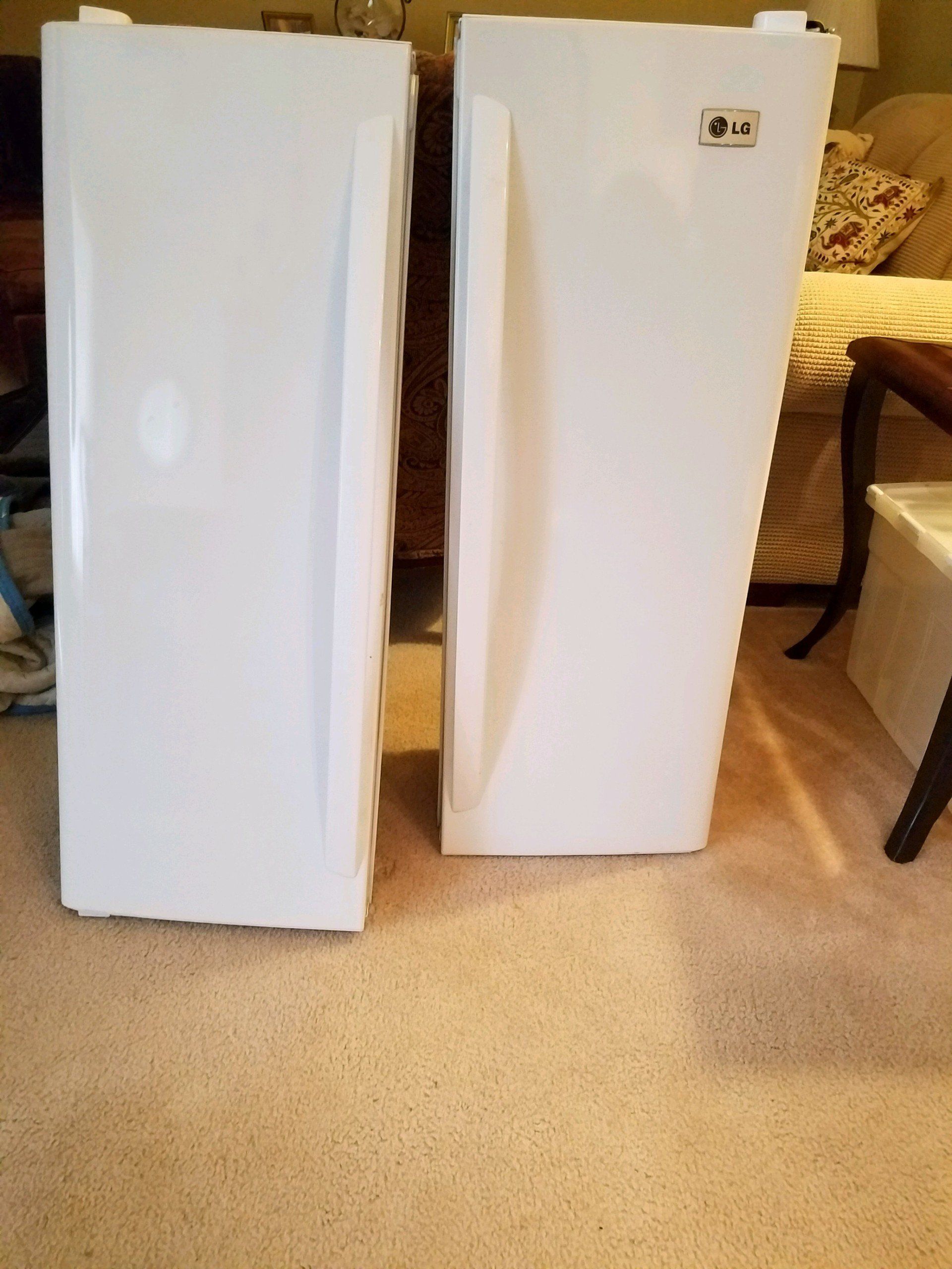 Two white refrigerators are sitting next to each other on a carpeted floor.
