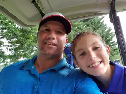 A man and a girl are posing for a picture in a golf cart.