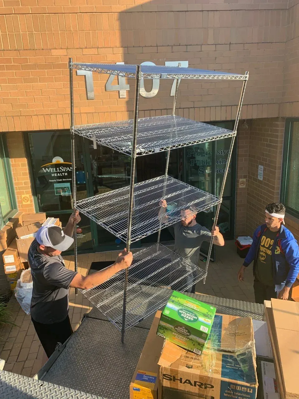 A group of men are working on a metal rack in front of a brick building.