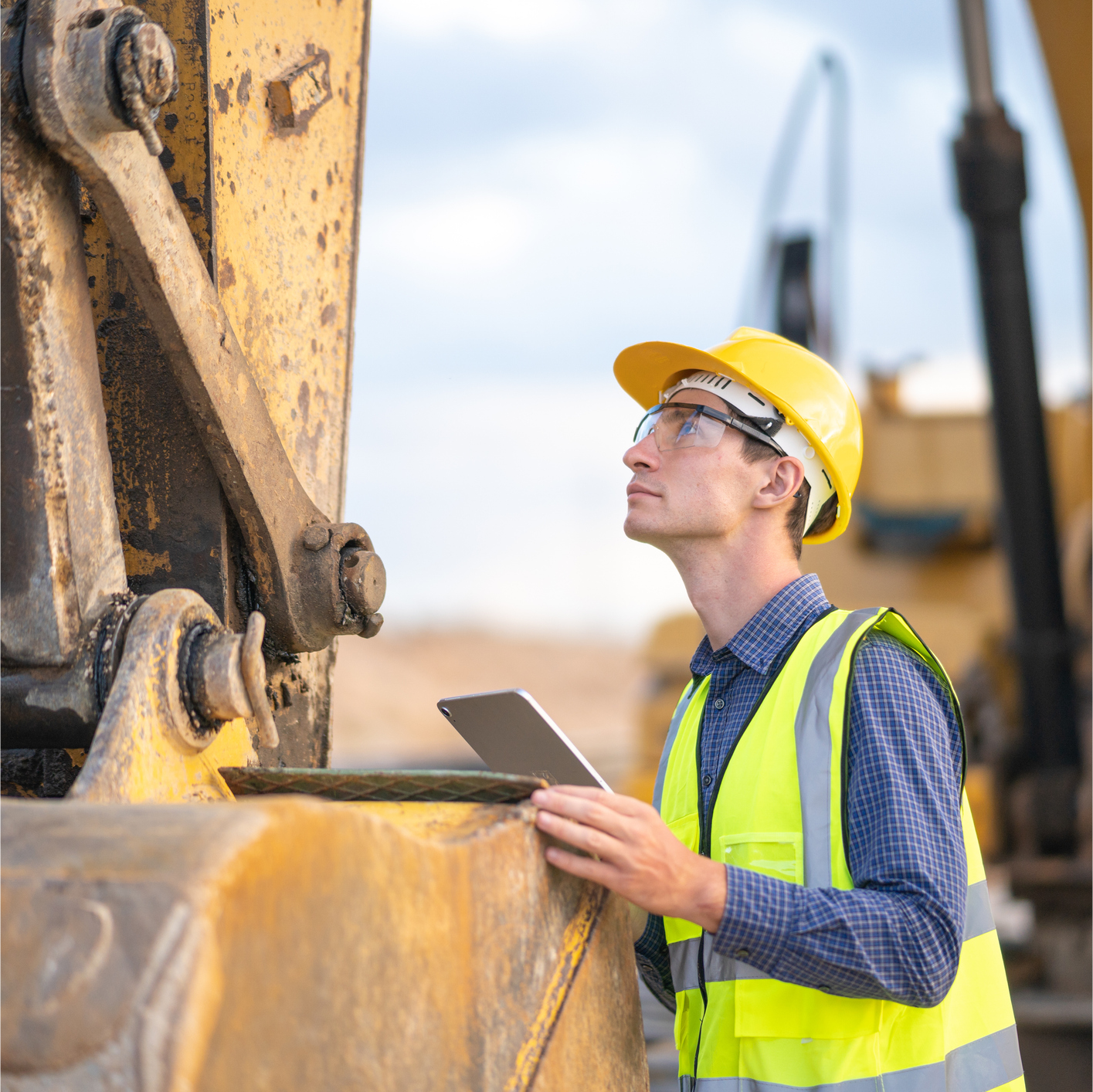 A construction worker is looking at a tablet while standing next to a bulldozer.