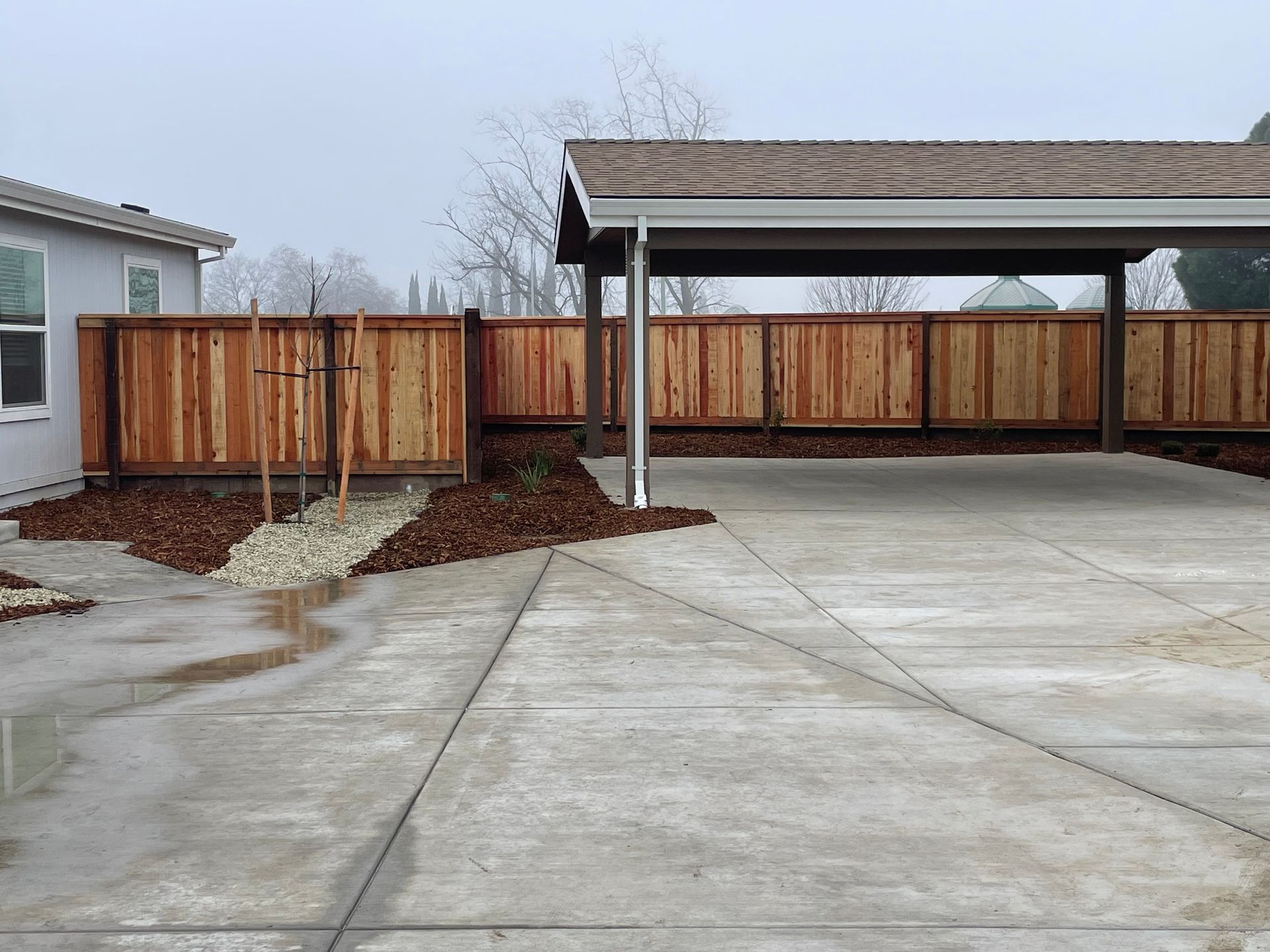 Green chain-link fence on a grassy hill, with trees in the background.