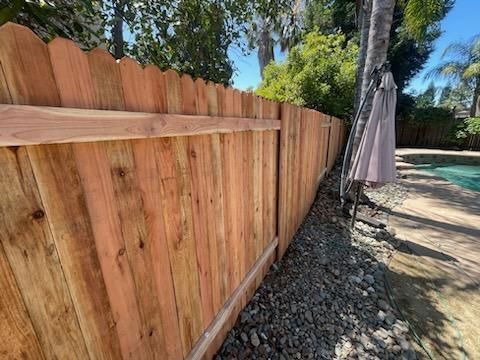 Wooden fence beside a pool, with rocks along the edge and trees overhead