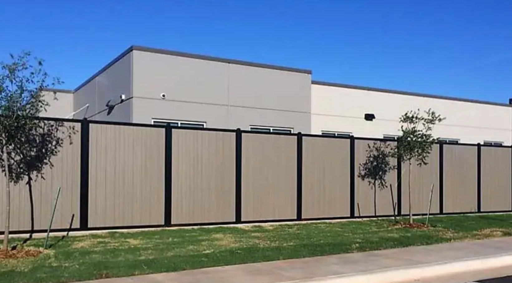 Beige privacy fence with black posts in front of a light gray building.
