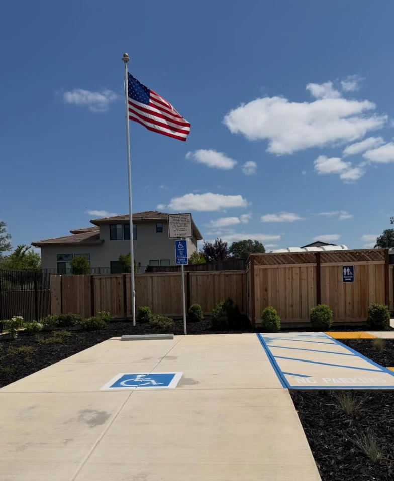 American flag flying over an accessible parking lot with a wooden fence and house in the background