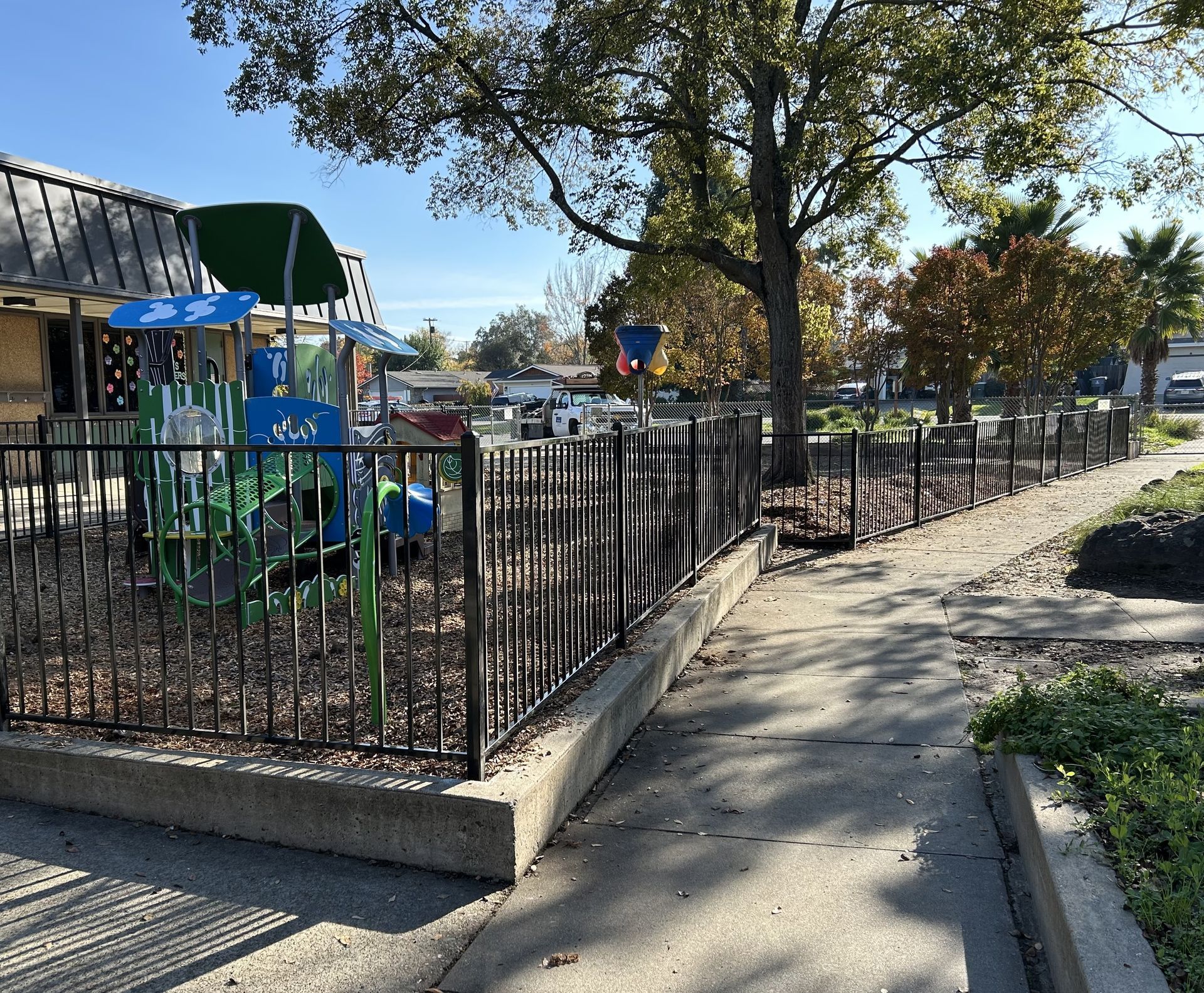 Black metal fence with arched top and spiked finials, in front of green bushes.