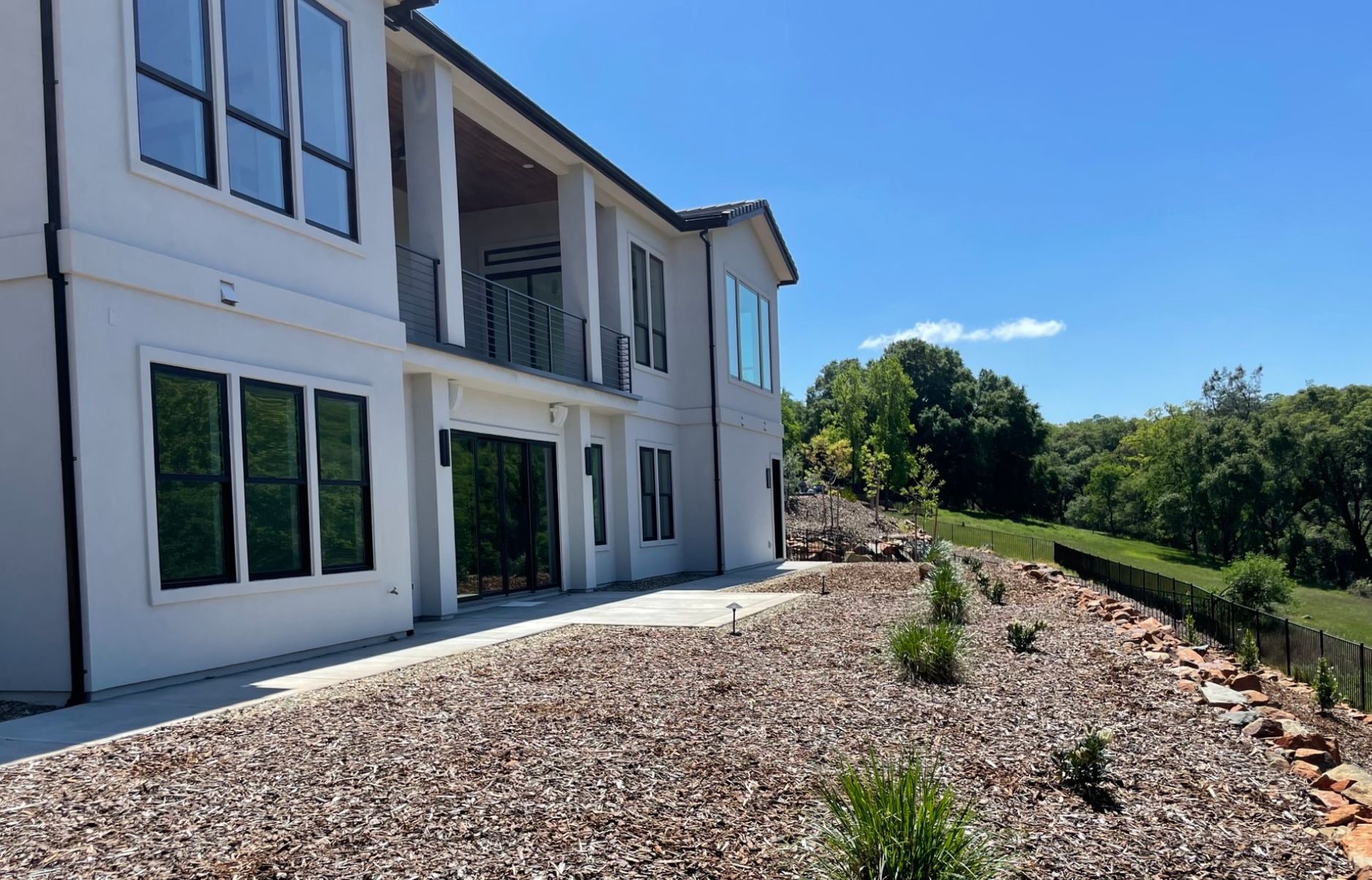 Exterior view of a white two-story house with black-framed windows, overlooking a hillside on a sunny day.