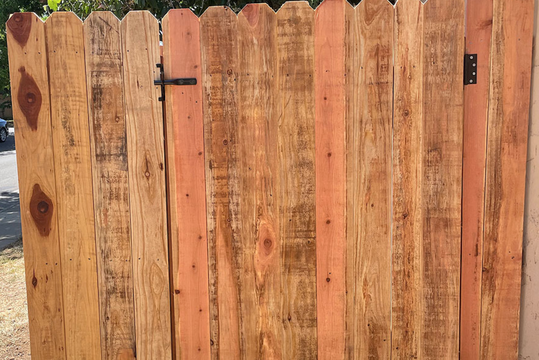 Wooden gate with uneven, vertical planks and black hinges.