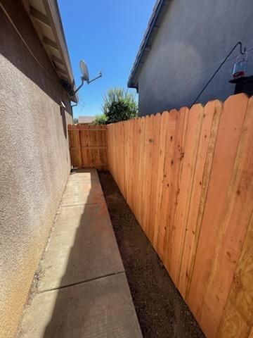 Narrow side yard with concrete walkway between a house and wooden fence under a clear blue sky