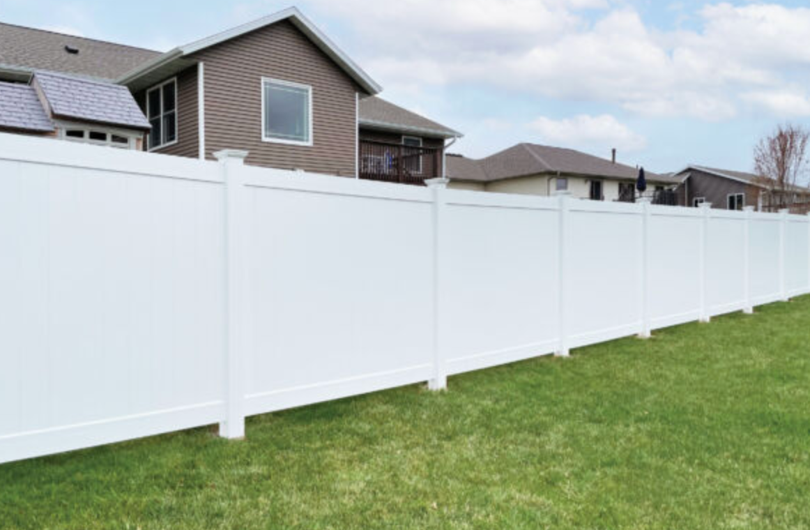 White vinyl fence in a grassy yard, with houses in the background under a blue sky.