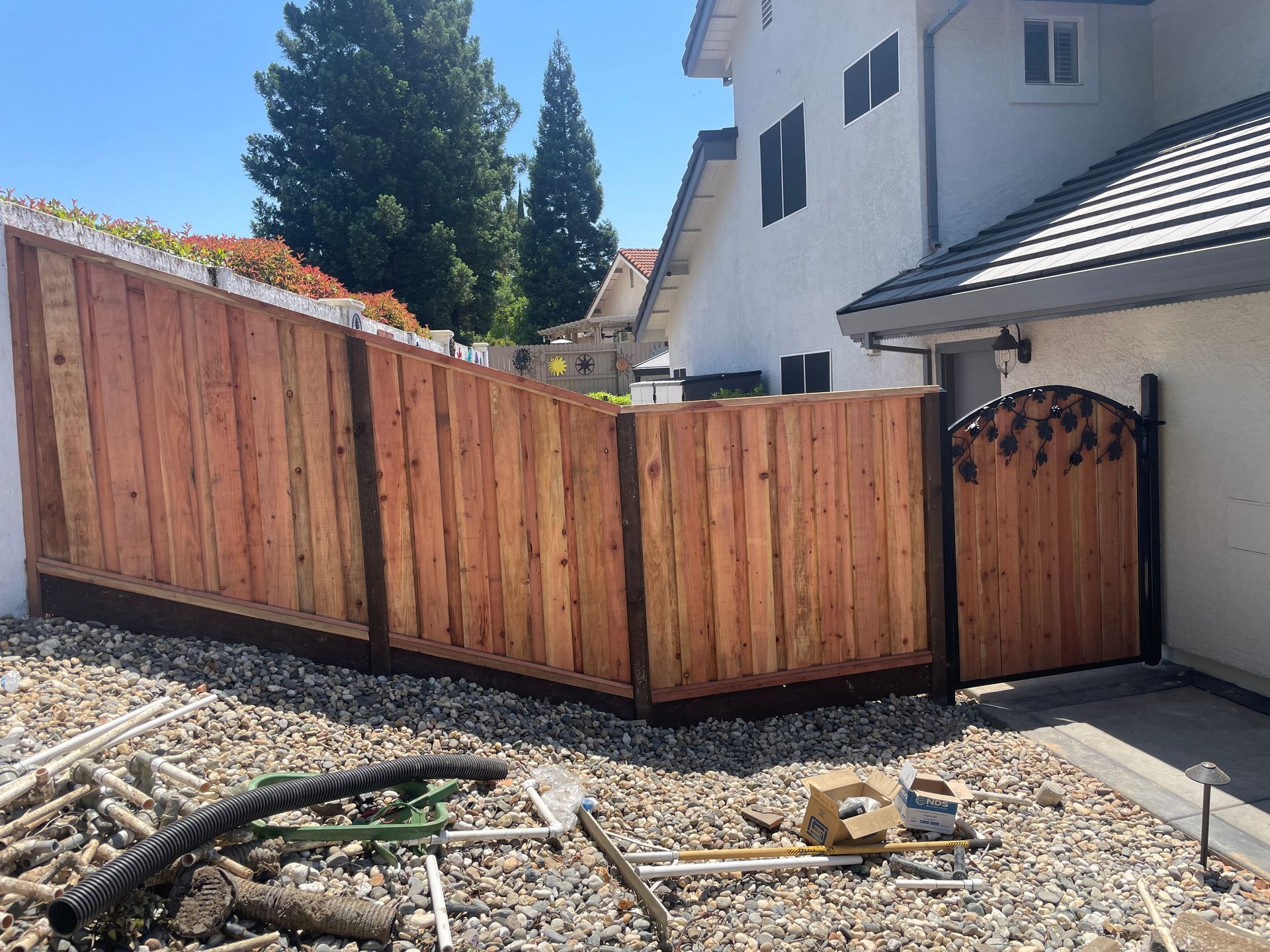Wooden fence and gate surrounding a yard with gravel, next to a white house.