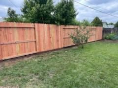 Wooden privacy fence beside a grassy backyard with a small tree under a cloudy sky