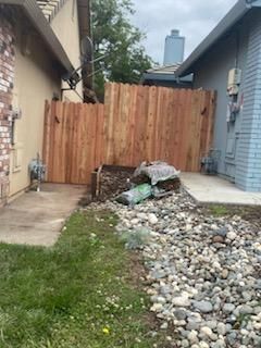 Backyard with piles of rubble and gravel beside two houses and a wooden fence