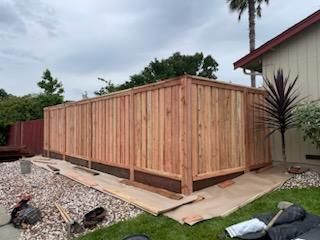 New wooden fence panels along a side yard beside a house, with construction materials on the ground.