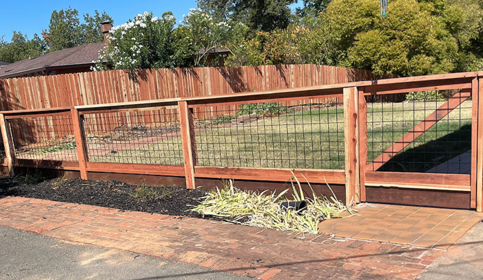 Wooden fence with black metal grid sections and gate, fronted by a brick path and mulch.