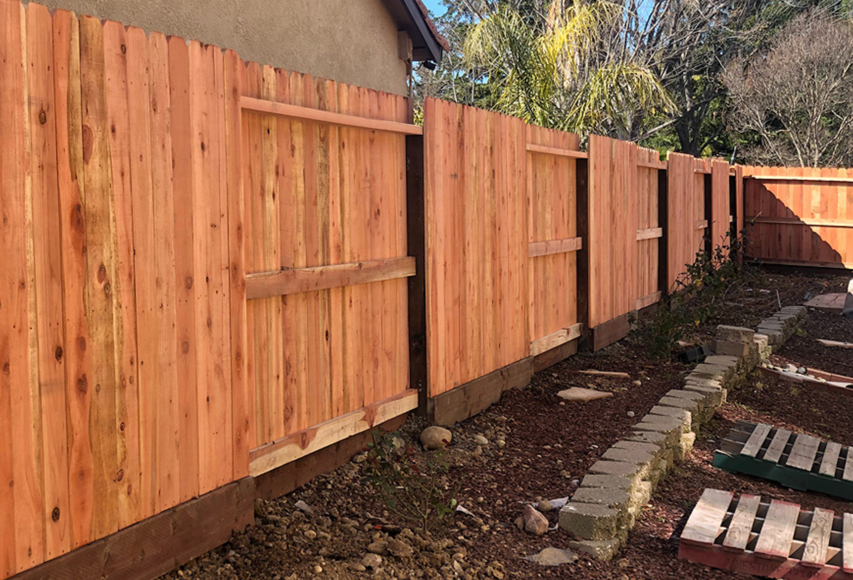 Newly constructed wooden fence in a yard, stained reddish-brown.