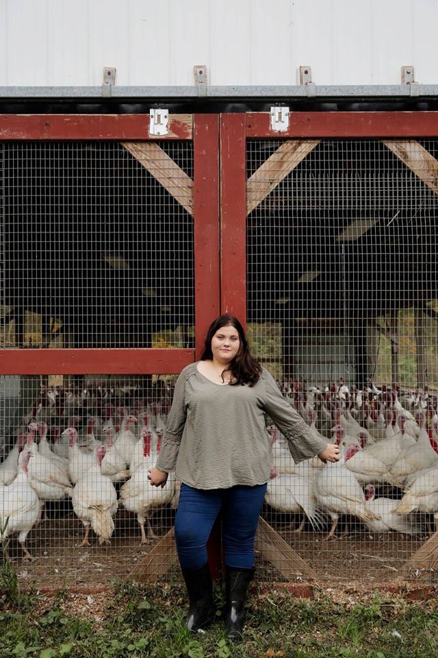 A woman is standing in front of a fence surrounded by turkeys.