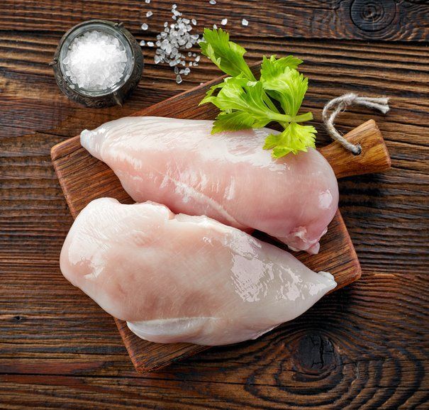 Two raw chicken breasts on a wooden cutting board on a wooden table.