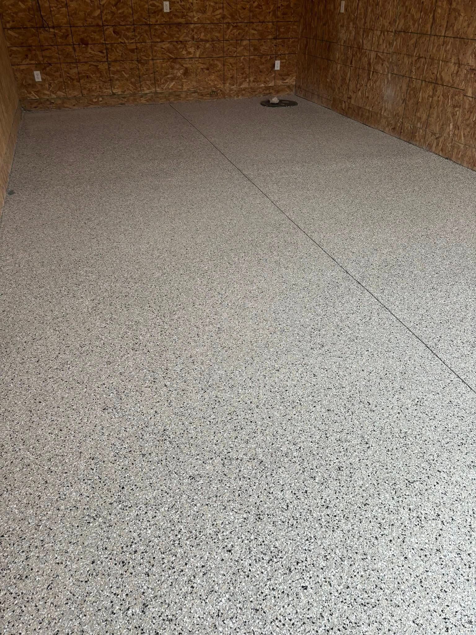 A newly installed gray and black speckled epoxy floor inside a garage with unpainted oriented strand board (OSB) walls.