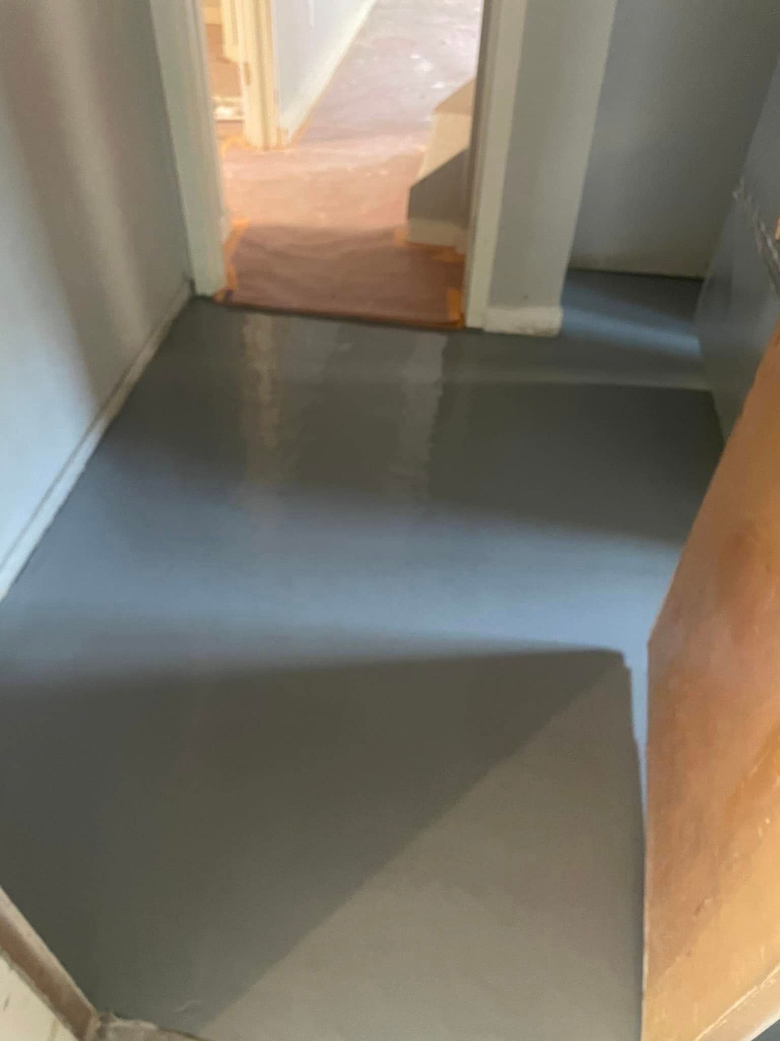 A newly painted, smooth light-gray floor inside a residential hallway with an open doorway leading to another room.