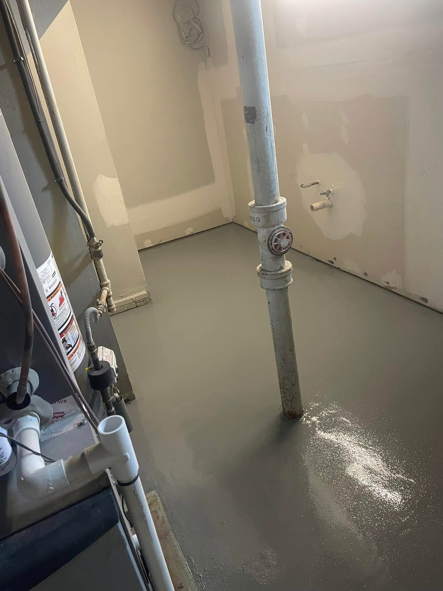 A grey epoxy-coated basement floor featuring a vertical plumbing pipe and partially finished drywall walls.