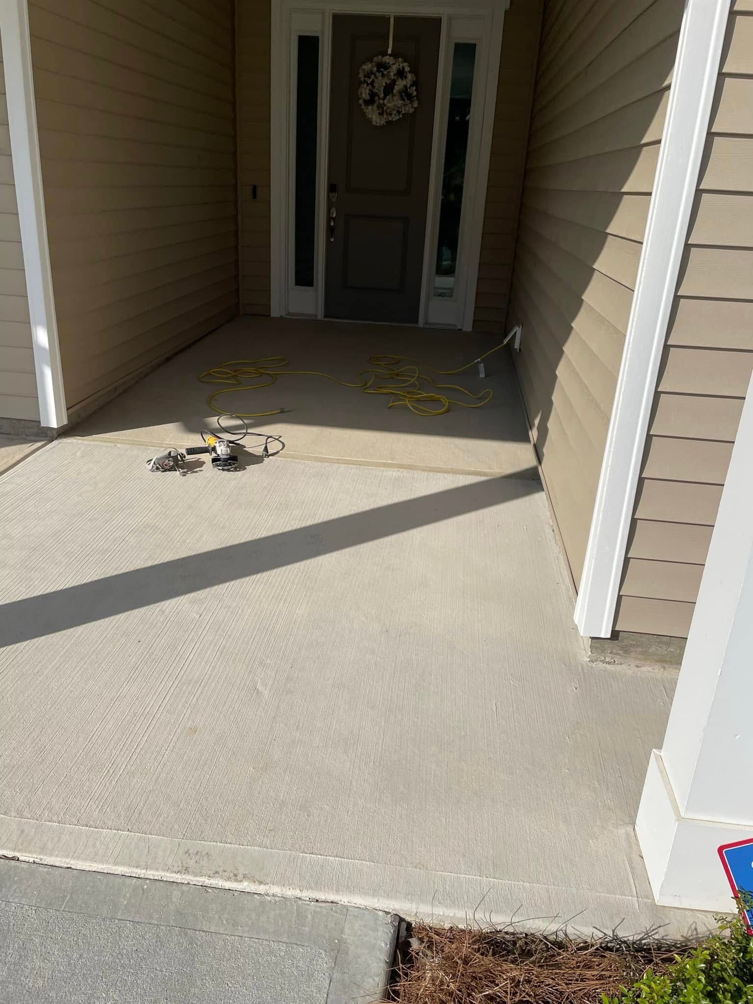 A front porch with tan siding and a dark brown door, featuring scattered yellow leaves on the concrete surface.