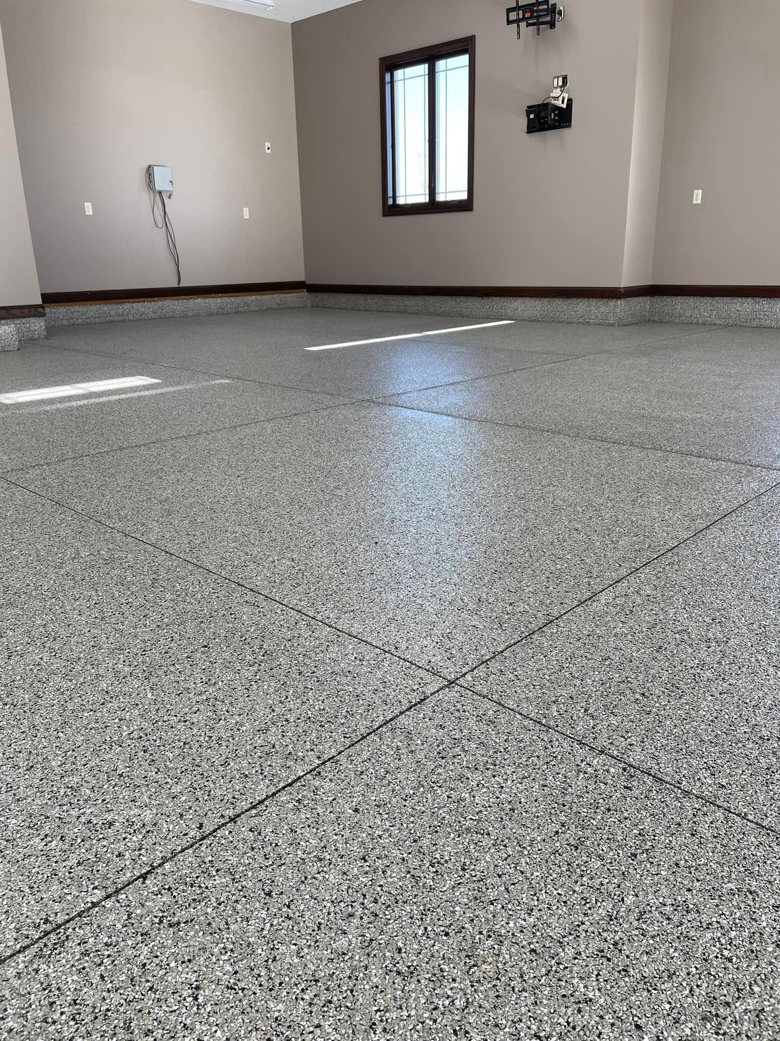 A garage interior featuring a glossy, light grey speckled epoxy floor with thin, dark grid lines.