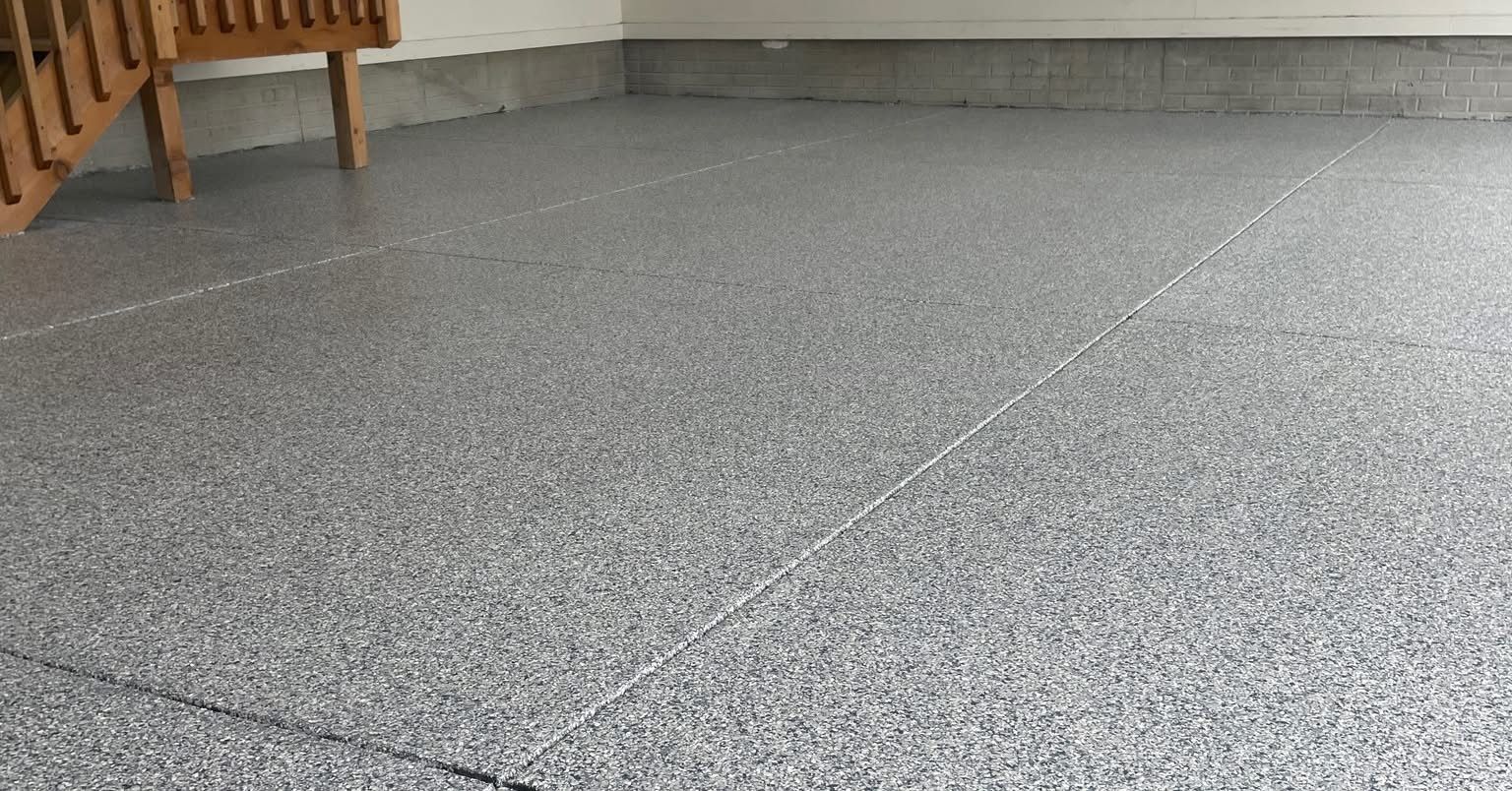 A garage floor featuring a gray and white speckled epoxy coating, with wooden stairs visible in the upper left corner.