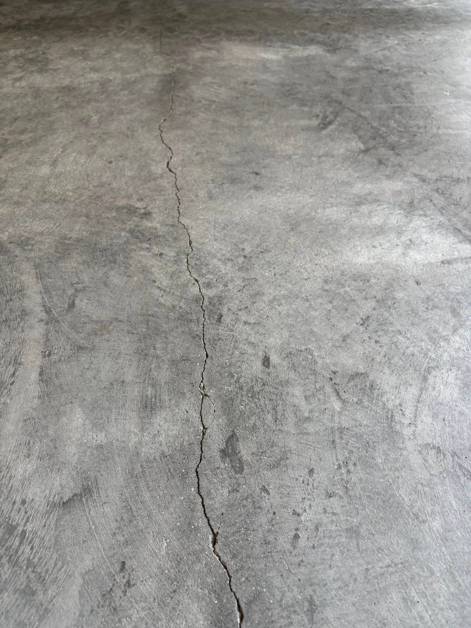 A vertical crack running through the center of a gray, textured concrete floor.