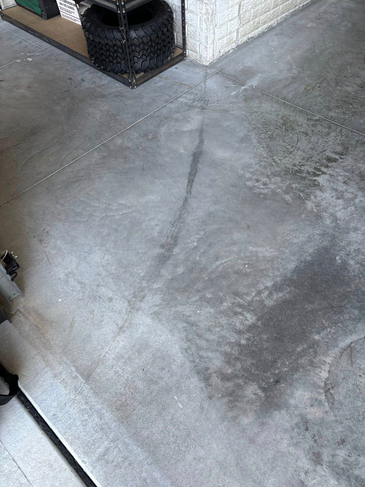 A dark, jagged crack runs across a grey concrete garage floor, extending from near a stack of tires toward the center.
