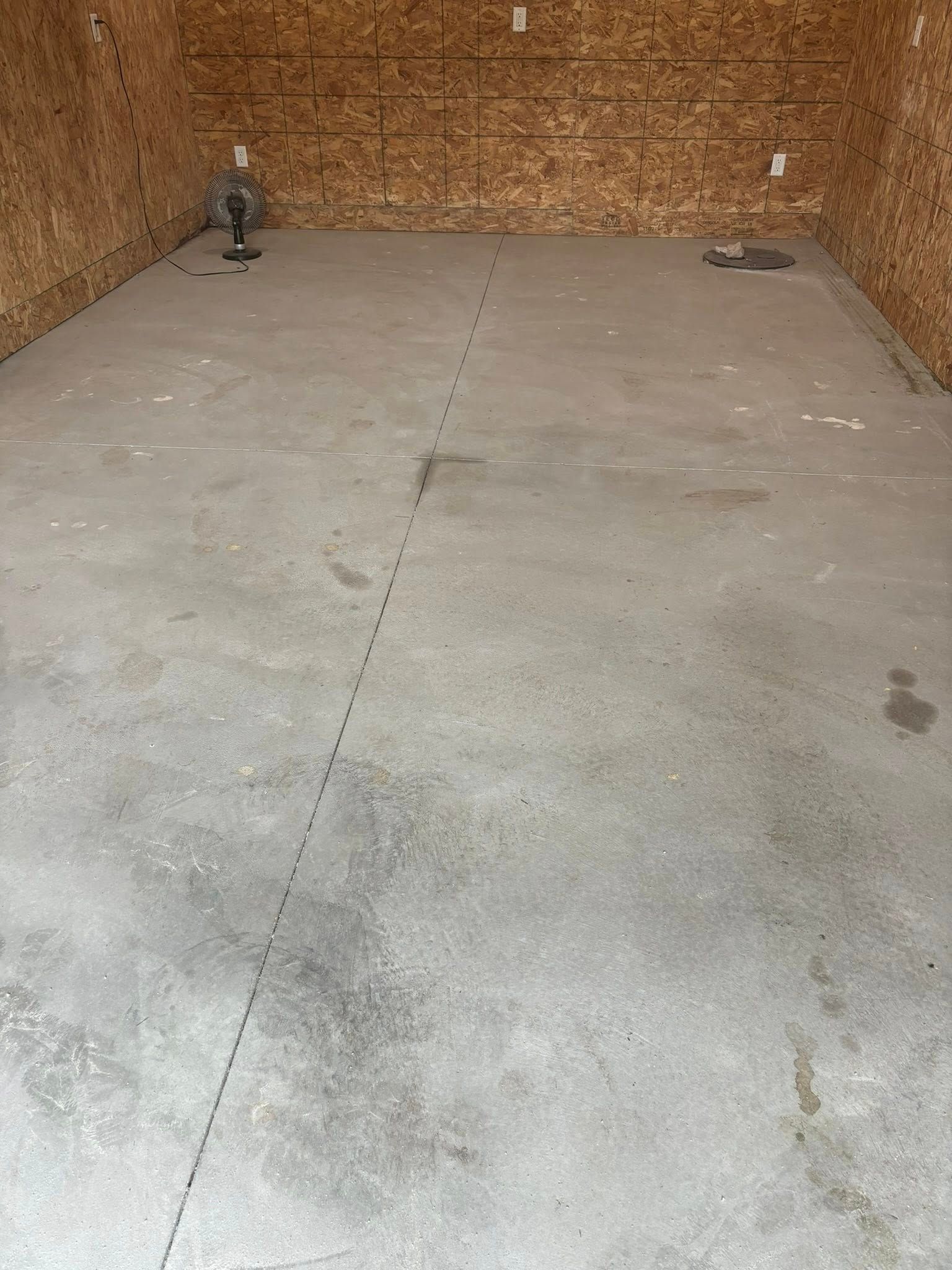 A gray concrete floor in an unfinished room with oriented strand board walls, featuring a dark seam line running down center.