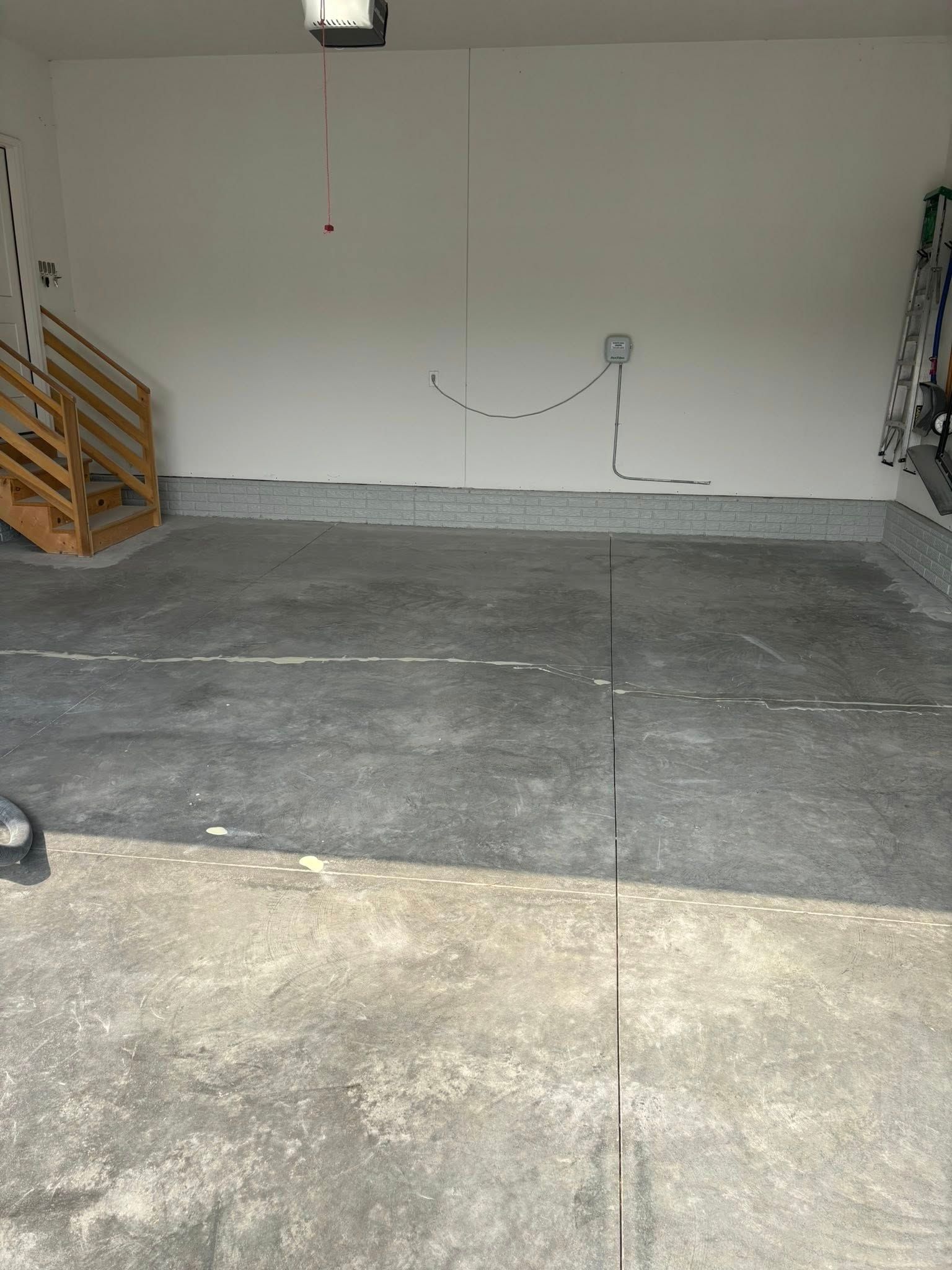 A garage interior with gray concrete floors, white walls, a wooden staircase, and a faint smiley face drawn on the wall.