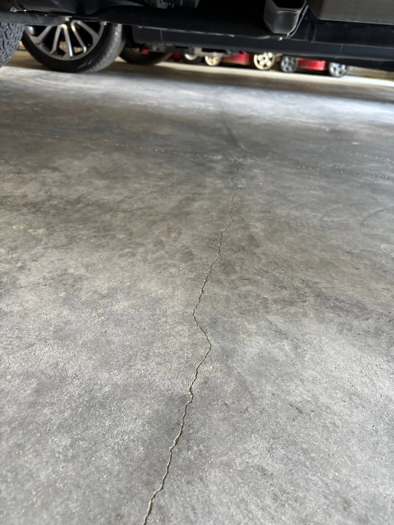 A thin, jagged crack runs vertically through a gray concrete garage floor beneath the parked chassis of a car.