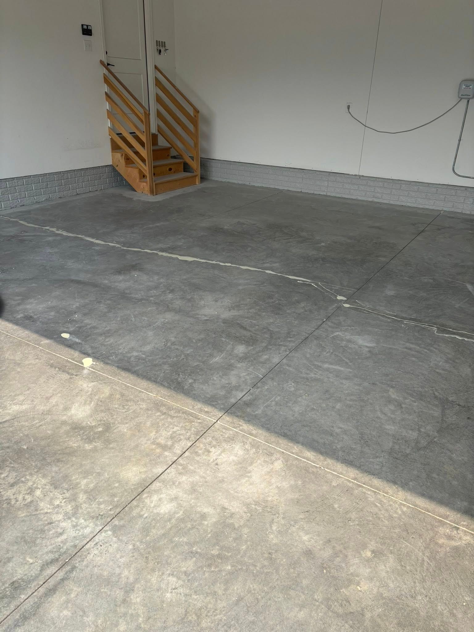 An interior garage space with light gray walls, a textured gray floor coating, and wooden stairs in the corner.