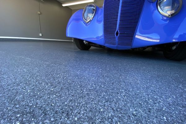 A bright blue vintage car parked on a gray, speckled epoxy garage floor.