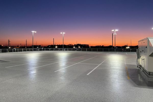 An empty rooftop parking lot with bright lights at dusk, showing a vibrant orange and purple sky.