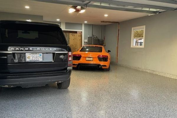 A black Range Rover and an orange Audi parked in a spacious garage with gray, speckled flooring.