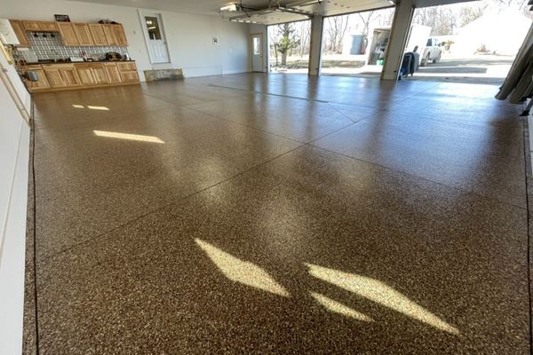 A spacious, clean garage featuring a glossy, brown-speckled epoxy floor and wooden cabinets along the side wall.