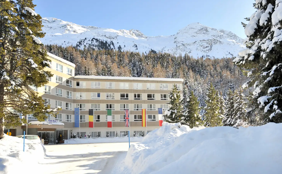 Hotel coberto de neve com bandeiras coloridas em frente a uma cordilheira.