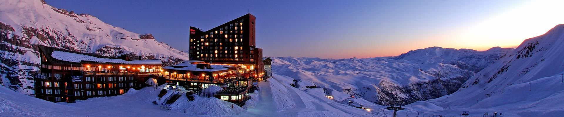 Uma paisagem montanhosa nevada ao entardecer, com um grande hotel iluminado.