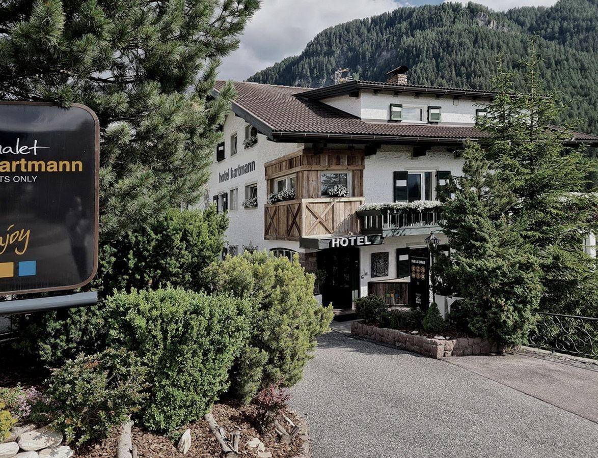 Prédio de hotel em frente a uma montanha, rodeado por árvores. Uma placa indica 