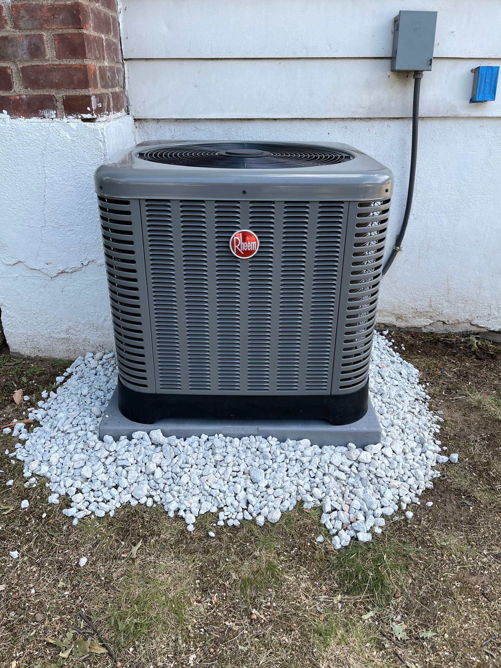 An air conditioner is sitting on top of a pile of gravel in front of a house.