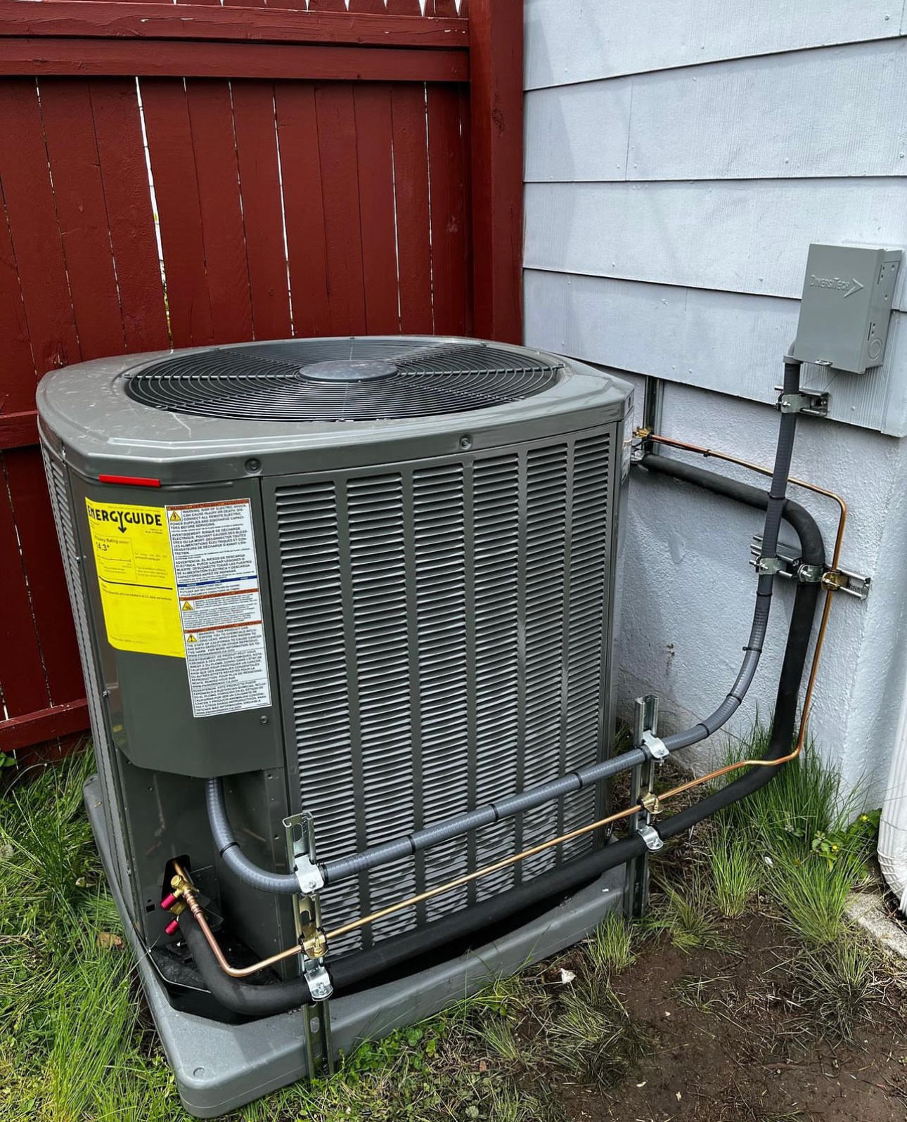 An air conditioner is sitting outside of a house next to a fence.