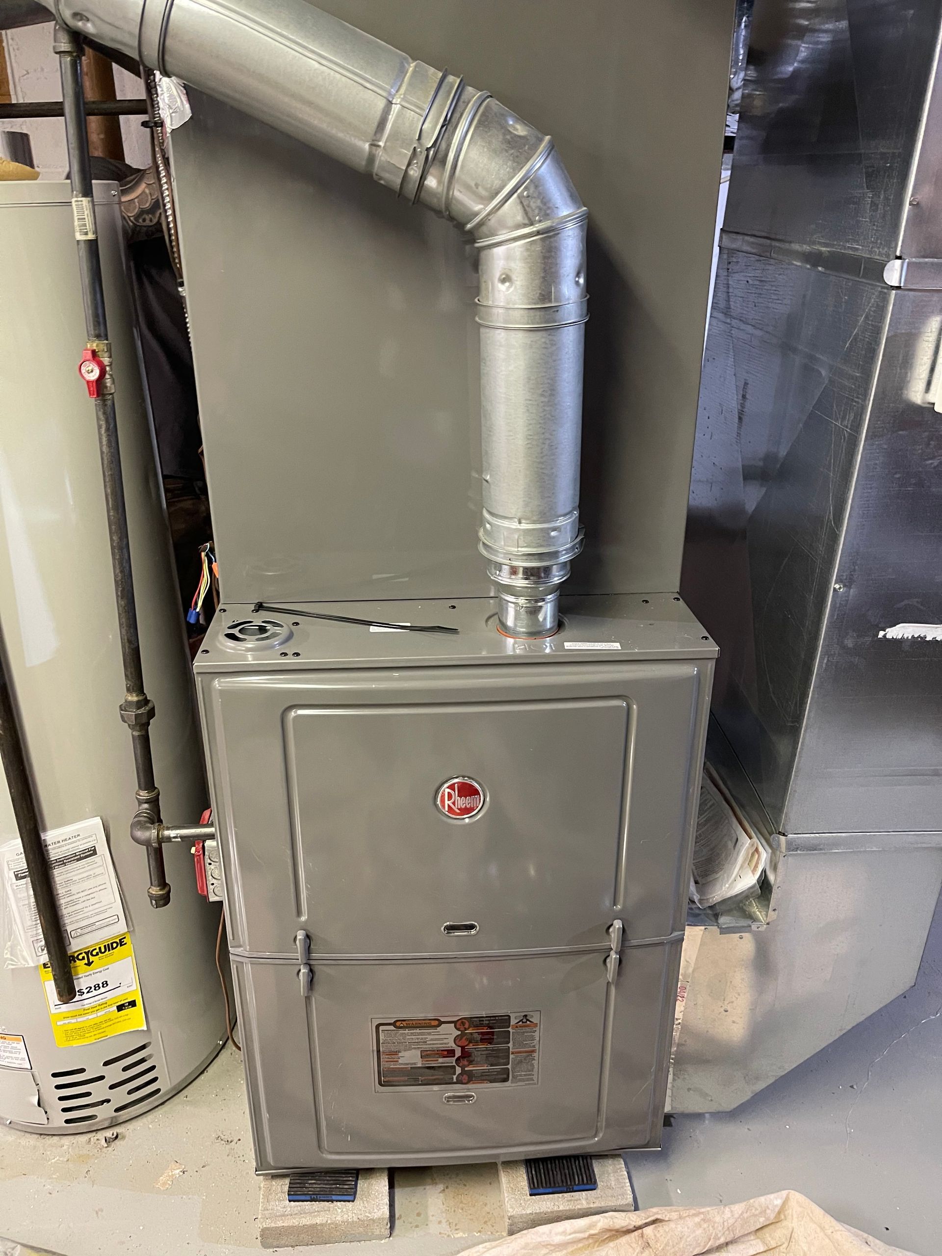 A furnace is sitting in a room next to a water heater.