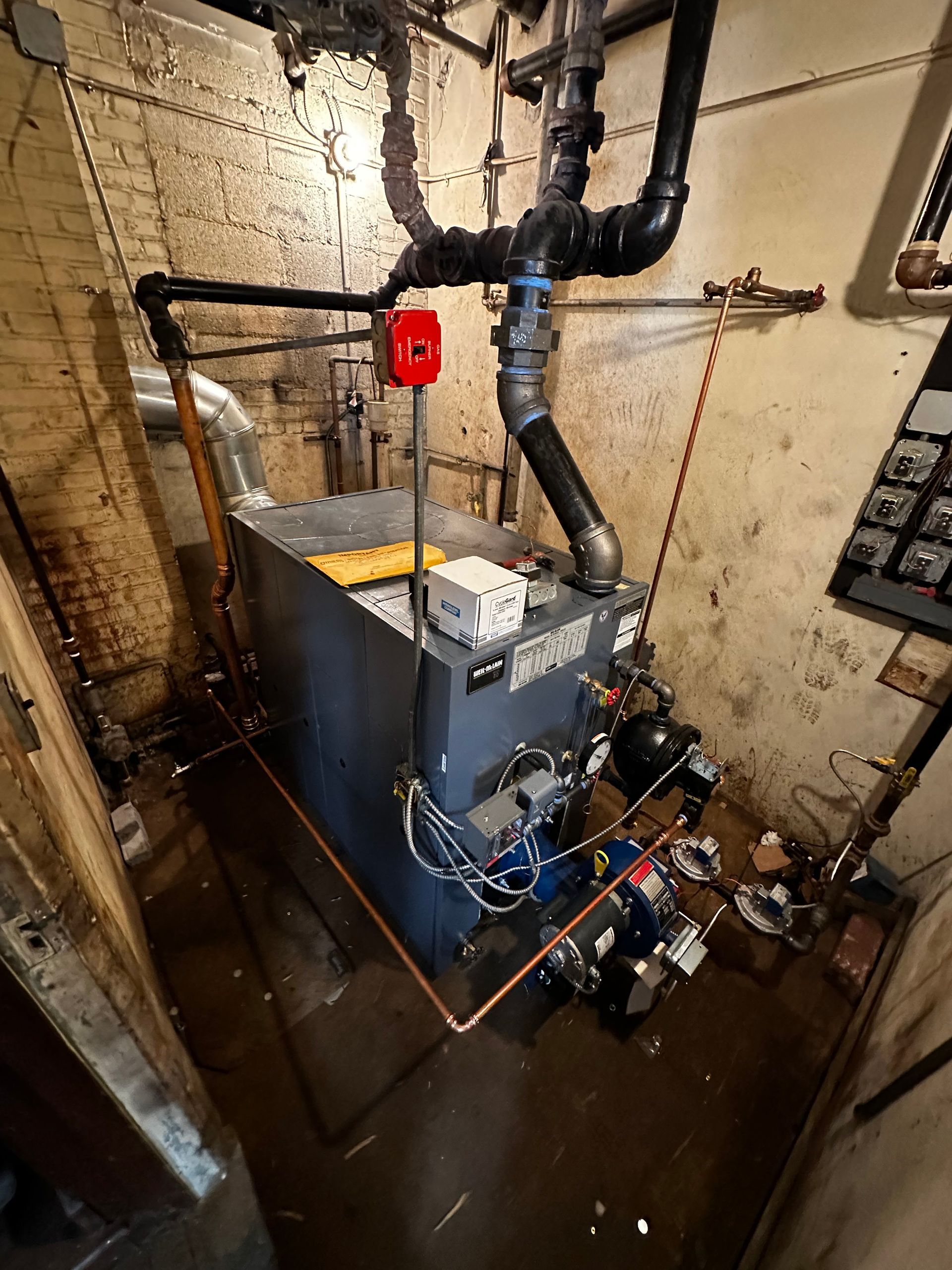 A large boiler is sitting in a basement next to a brick wall.