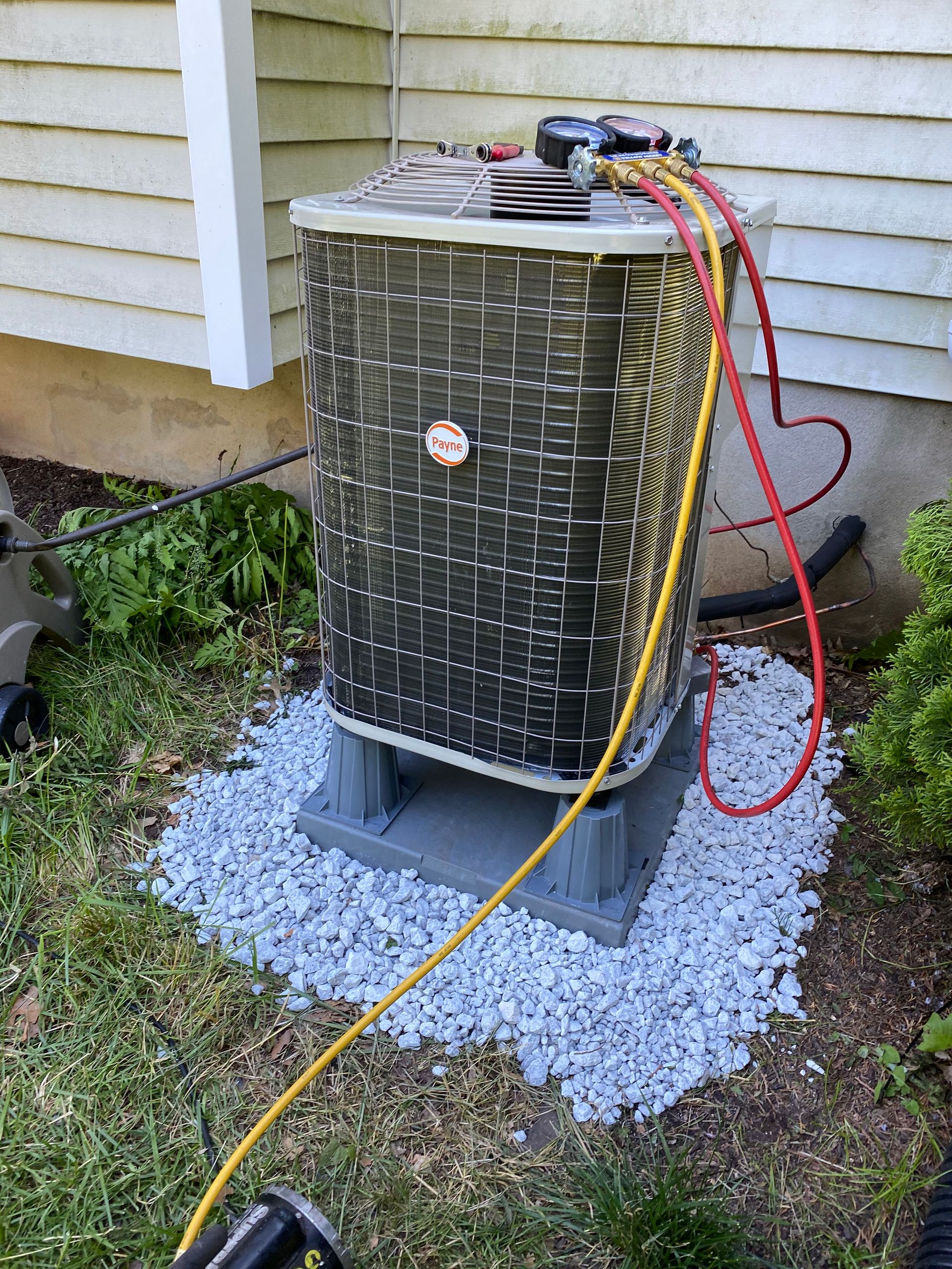 An air conditioner is sitting on top of a pile of gravel next to a house.