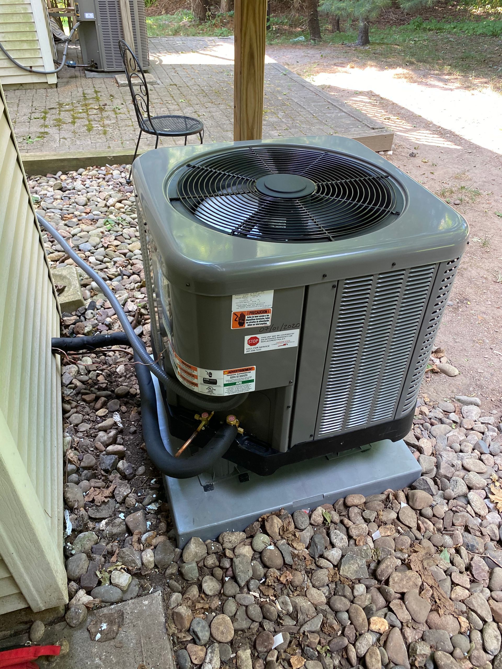 A large air conditioner is sitting on top of a pile of rocks next to a house.