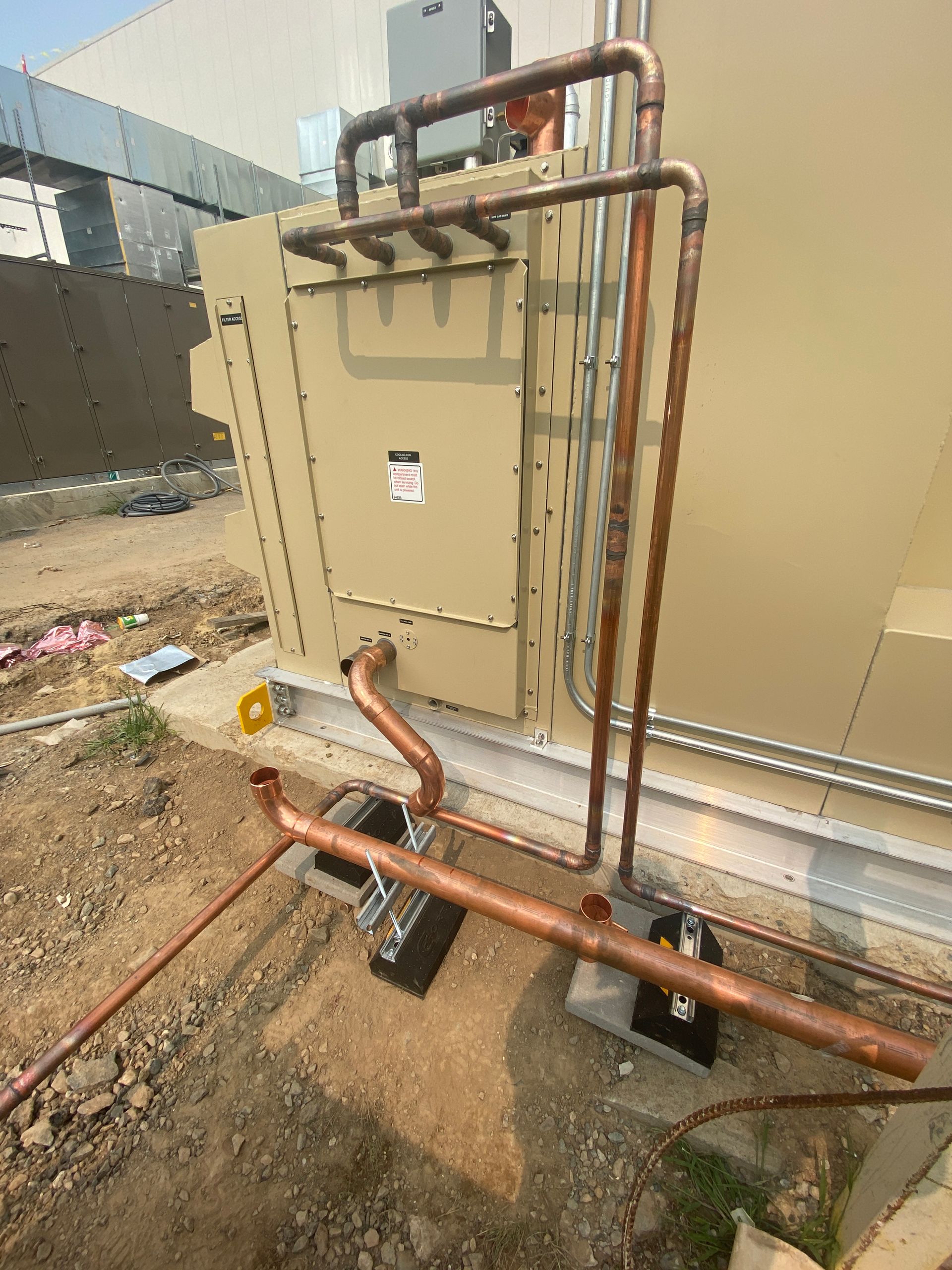 A building with copper pipes attached to it is sitting on top of a dirt field.
