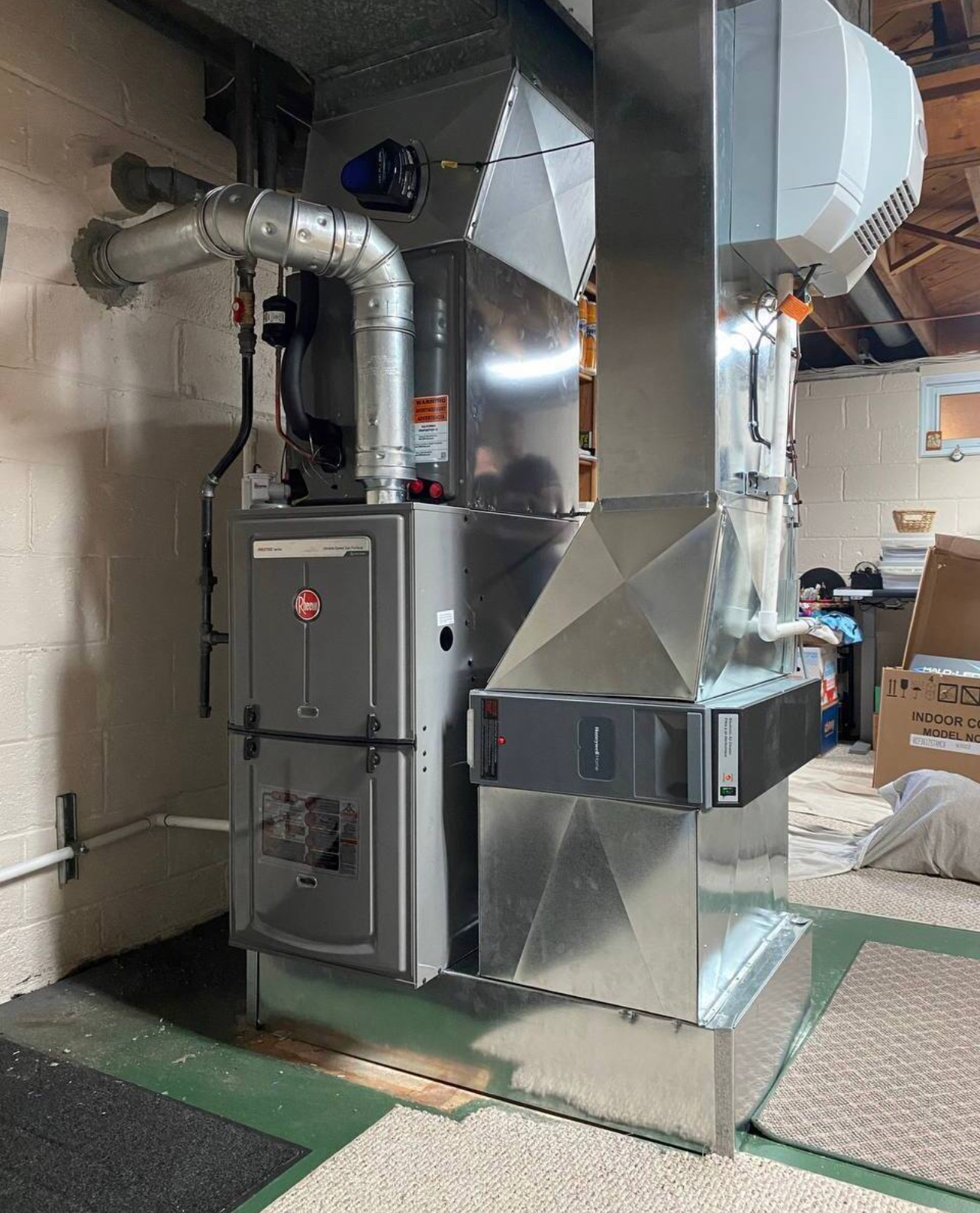 A stainless steel furnace is sitting in a basement next to a brick wall.